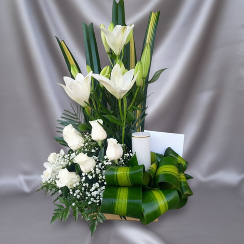 Arreglo floral vertical con lirios blancos altos, rosas blancas y follaje verde sobre tela gris