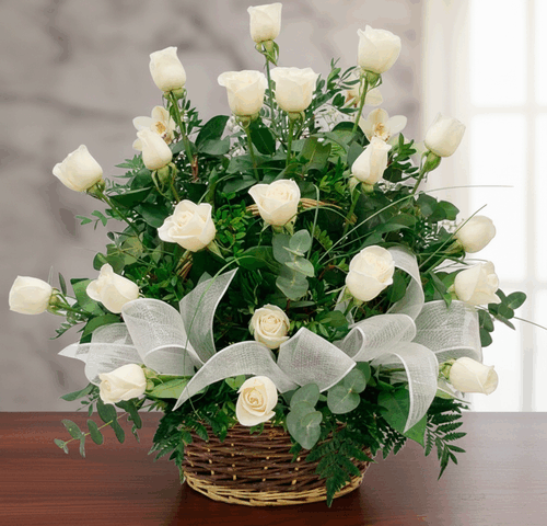 arreglo de rosas blancas con follaje verde en canasta de mimbre sobre mesa de madera