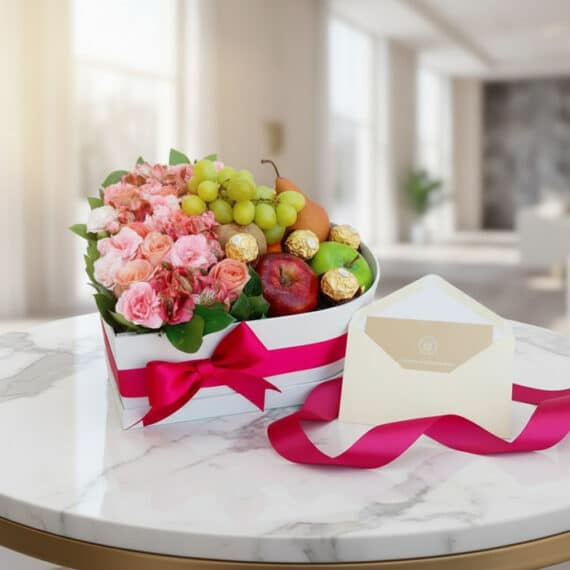 Arreglo floral AMOS en caja corazón con rosas, alstroemerias, frutas frescas y chocolates Ferrero Rocher, sobre mesa de mármo