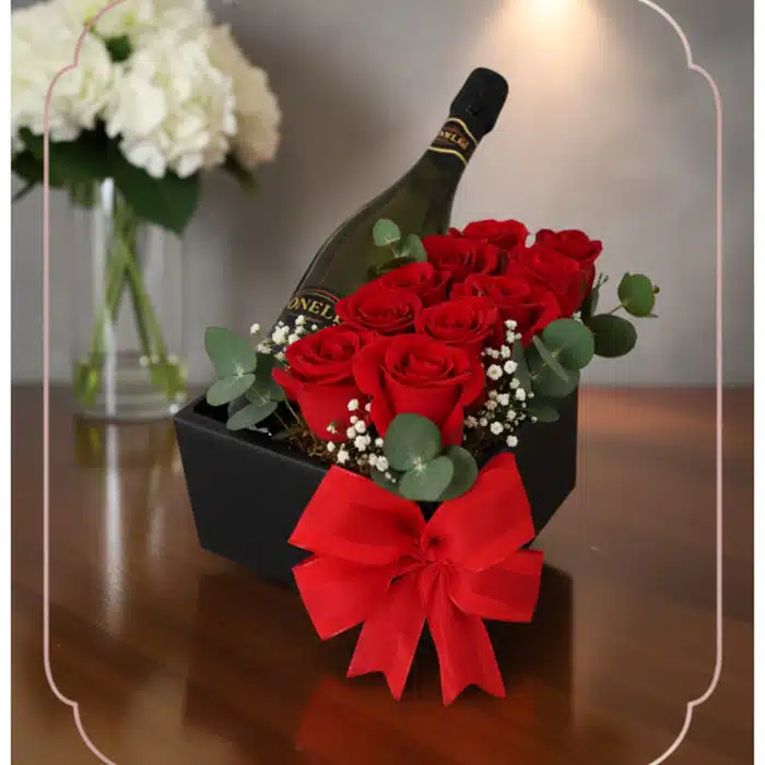 Arreglo floral NATALE con rosas rojas frescas, vino espumoso y lazo rojo en caja negra, ideal para regalo elegante.